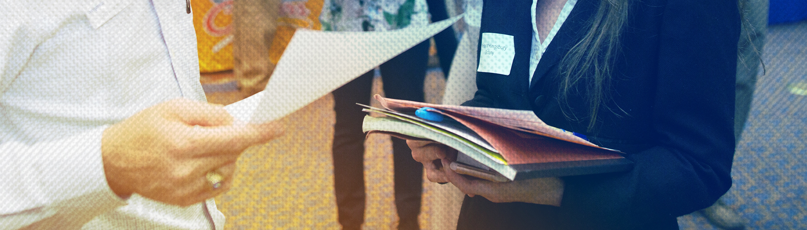 Cropped image of an employer's hands holding papers and a student's hands holding a notebook. 